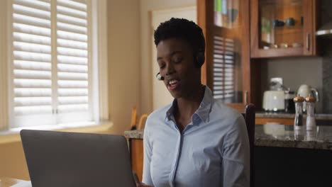 Mujer-Afroamericana-Con-Auriculares-De-Teléfono-Haciendo-Una-Videollamada-En-Una-Computadora-Portátil-Mientras-Trabaja-Desde-Casa