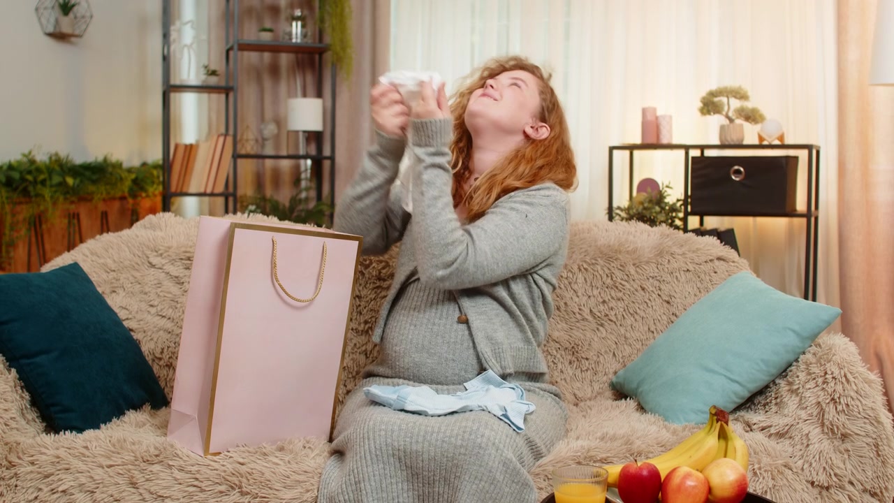 Pregnant woman unpacking shopping bags with baby clothes excited and satisfied with new purchases