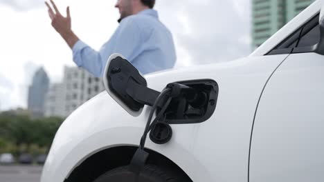 Suit-clad-businessman-with-progressive-ambition-leaning-on-his-electric-vehicle.