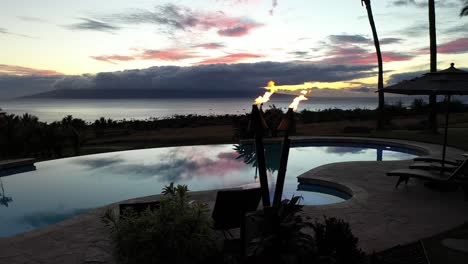 drone parallax around infinity pool deck with torches burning during colorful sunset