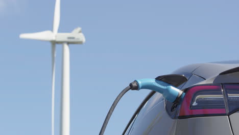 a generic electric car charges in front of a wind turbine, sunny day