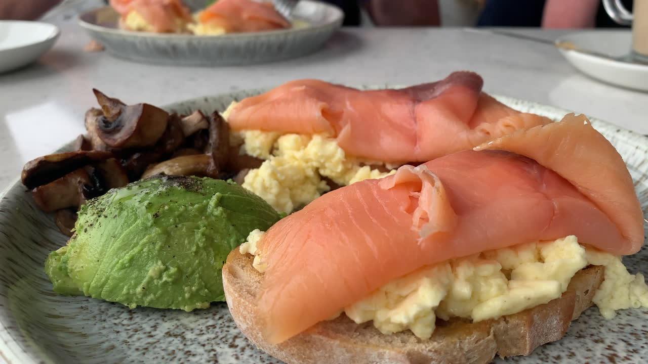 Colazione con bruschetta di avocado e salmone, uova e funghi in un caffè ristorante
