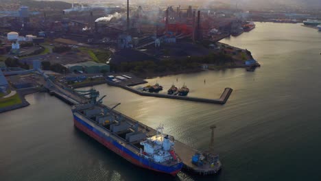 Crane-Ship-And-Jetty-On-Water-Surface-At-Port-Kembla-In-Wollongong,-Australia-With-Industrial-Plant-In-Background