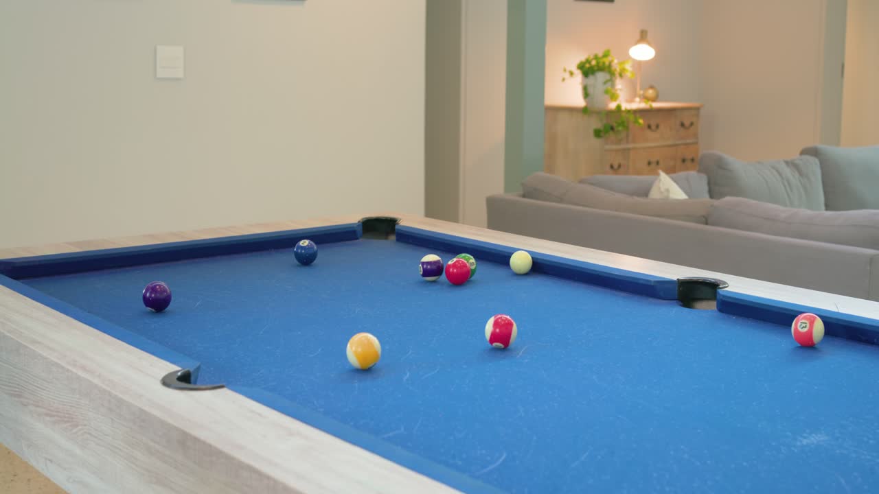 Male with dreadlocks lining up and striking shot at home on blue-felt pool table and celebrating