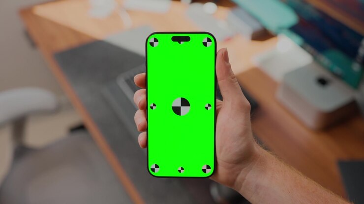 Persona che tiene uno smartphone con schermo verde in un ambiente di lavoro moderno, lo schermo si spegne