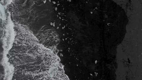 aerial shot along the sea front on a black sand beach covered in icebergs