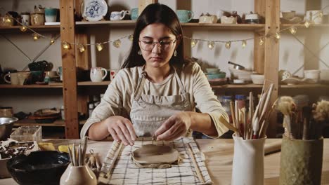 young woman potter makes patterns of the piece of clay using stamping