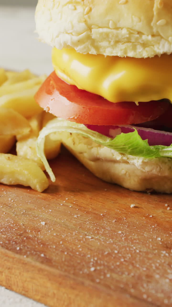 video de una hamburguesa con queso, papas fritas y un cuenco de ketchup en una tabla de madera
