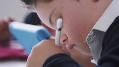 un escolar con síndrome de down usando un lápiz y una tableta en una clase de escuela primaria, de cerca, vista lateral