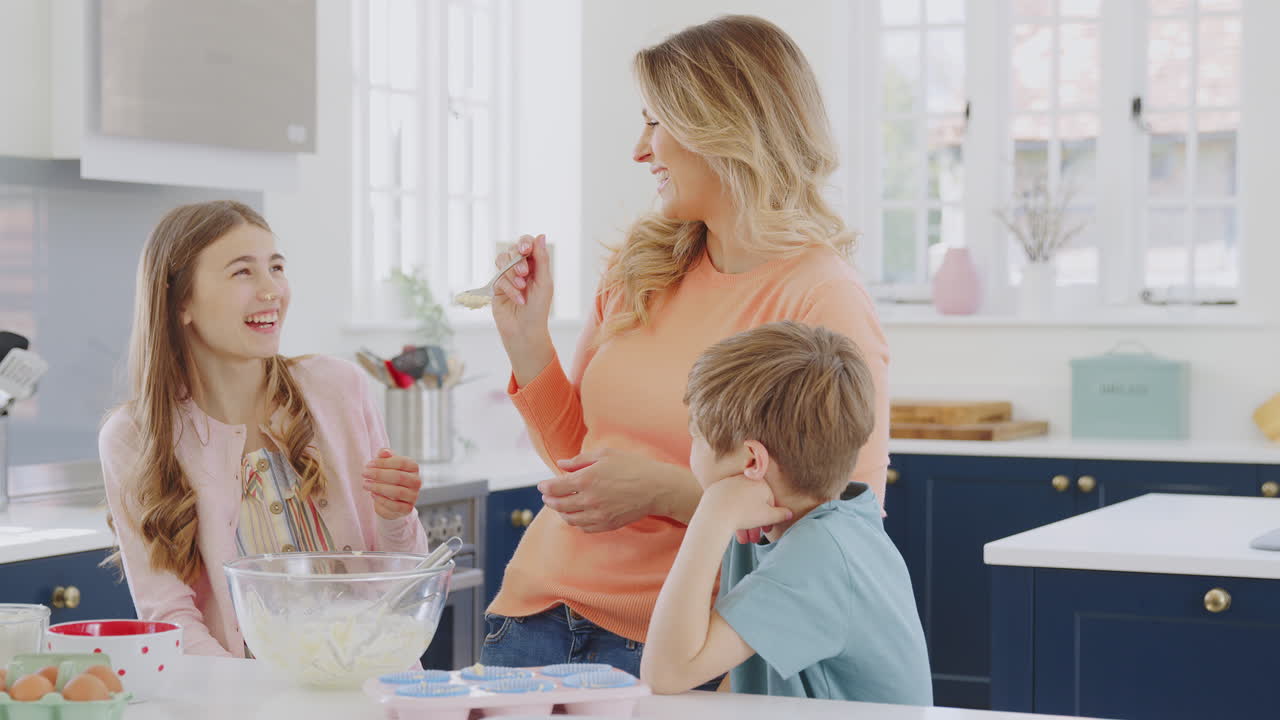 Mother Putting Cake Mixture On Daughter's Nose In Kitchen As They Have Fun Baking Cakes Together