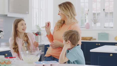 mother putting cake mixture on daughter's nose in kitchen as they have fun baking cakes together