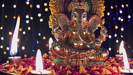 a low-angle video shot of a ganesha statue surrounded by candles and petals, with bokeh lights