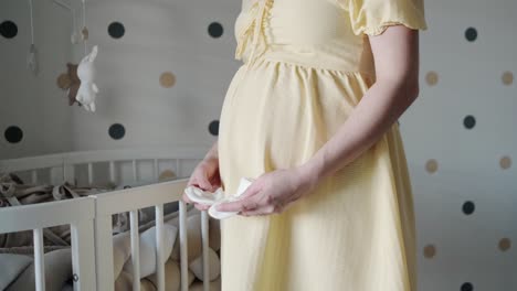 pregnant woman standing next to wooden crib holding baby sock it her hands