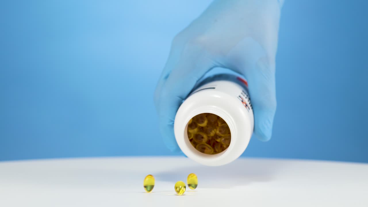 파란 장갑을 쓴 손이 오메가 비타민  ⁇ 을 비우고, 파란 바탕의 스튜디오