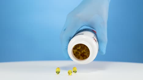 mano con guante azul vacía cápsulas de vitaminas omega, estudio con fondo azul