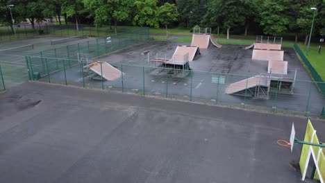 Vista-Aérea-Volando-A-Través-De-La-Rampa-Del-Parque-De-Patinaje-Cercado-Y-La-Cancha-De-Baloncesto-En-Un-Patio-De-Juegos-Vacío-Y-Cerrado