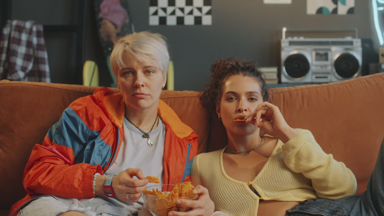 Bored Girls Eating Chips and Watching TV on Couch in Living Room