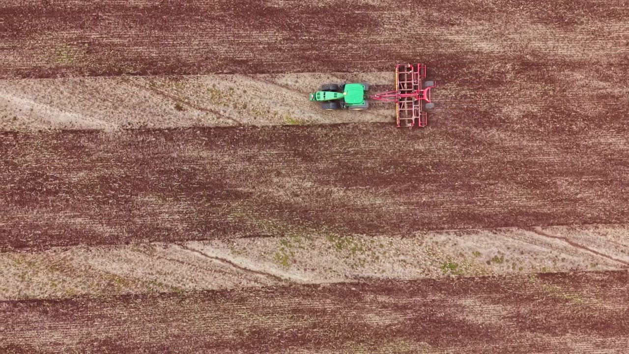 Trattore ara il campo, preparando il terreno per la semina in zona rurale di giorno con cieli sereni e tracce visibili nel terreno