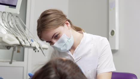 joven dentista en máscara acercándose con herramientas. lámpara dental se enciende en la boca de un paciente. de pie sobre un paciente