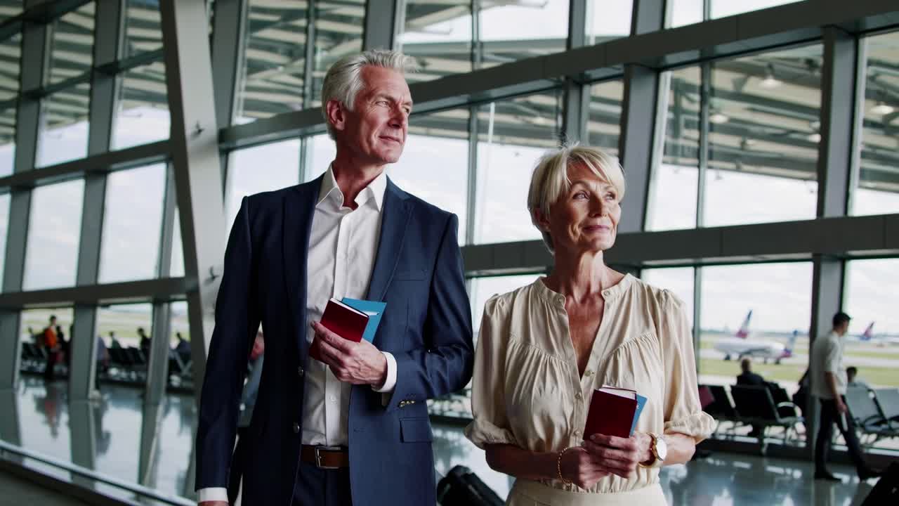 A video still of a mature couple at an airport, holding passports