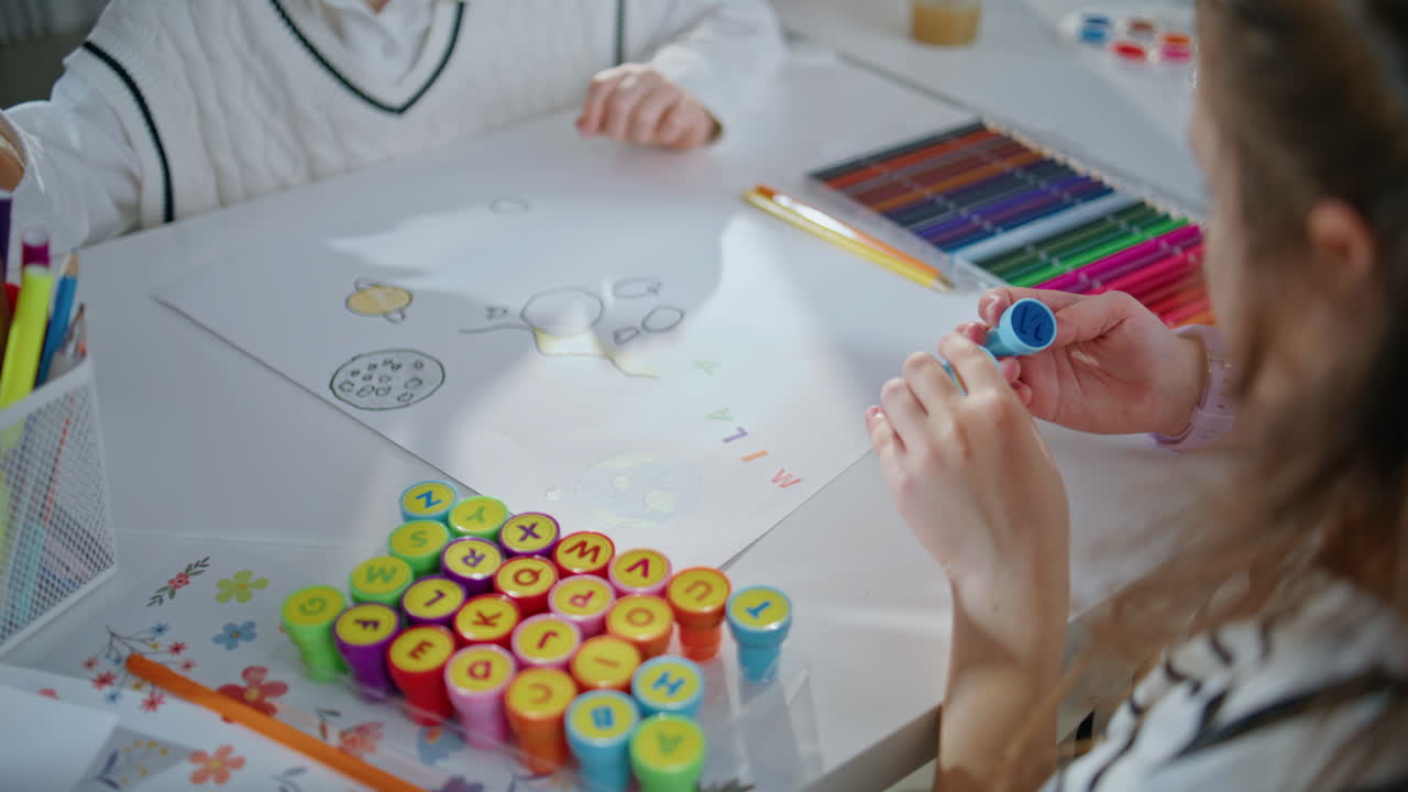 Small child examining stamp creating art in school closeup. Schoolgirl drawing