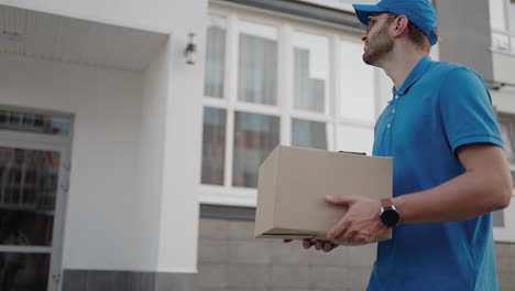 young delivery man wearing glasses and gloves holding box use phone walking on street quarantine outdoor shopping package pandemic postman self isolation slow motion