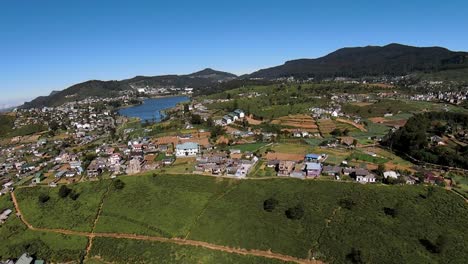 areal slide shot revealing green panoramic landscape of nuwara elya tea fields and glory gregory blue lake, sri lanka