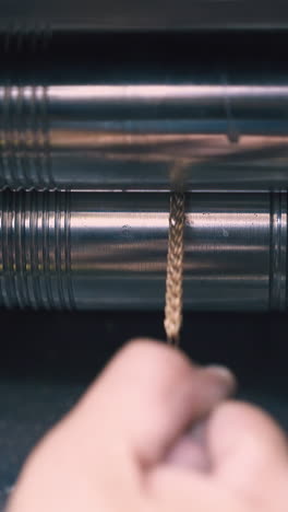 cu: professional goldsmith forge-rolls shiny gold chain with machine tool at workplace in light workshop closeup