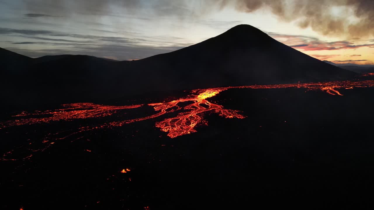 Fiume di lava incandescente che scorre lentamente su un vecchio campo di lava nella luce fioca del tramonto.