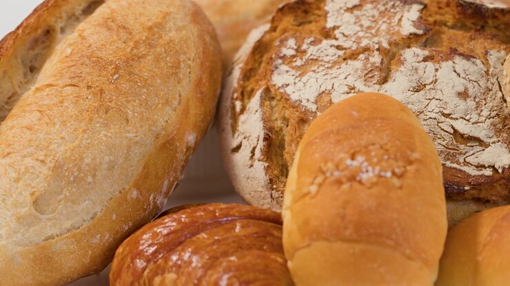 A hand reaches into a variety of crusty sourdough and multigrain loaves on white background.
