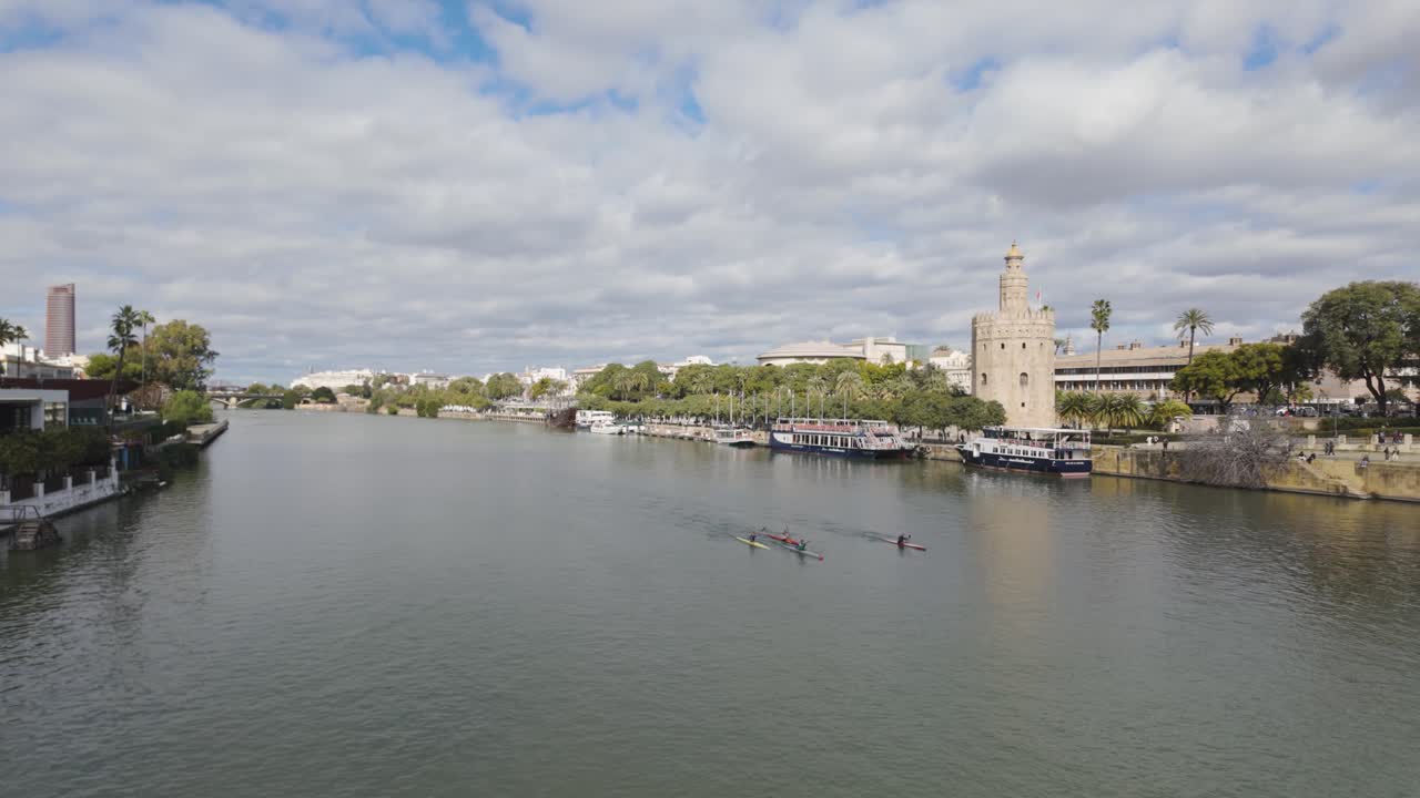 Panoramic view of Seville’s Guadalquivir River and Torre del Oro, with rowers in the water, Spain