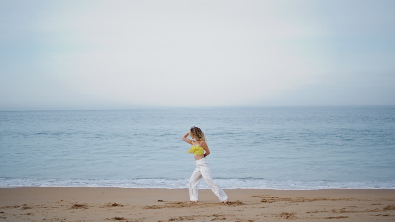 여자 댄서가 모래 해변에서 즉흥적으로 춤을 추고 있다. 여자 안무가 춤을 춘다.