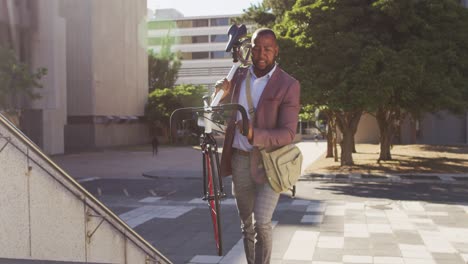 Happy-african-american-man-carrying-bike-upstairs-in-city