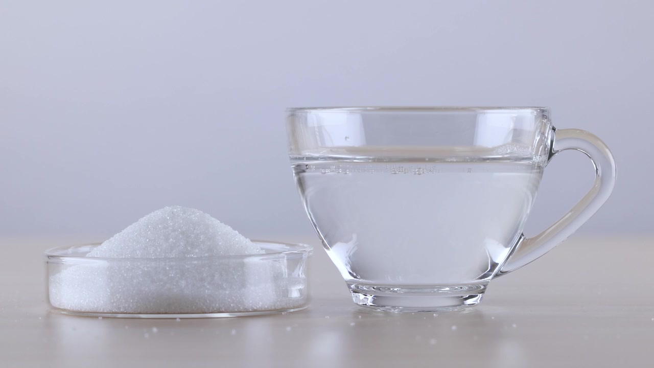 Granuli di zucchero bianco e acqua limpida si versano contemporaneamente in una capsula di Petri e una tazza di vetro