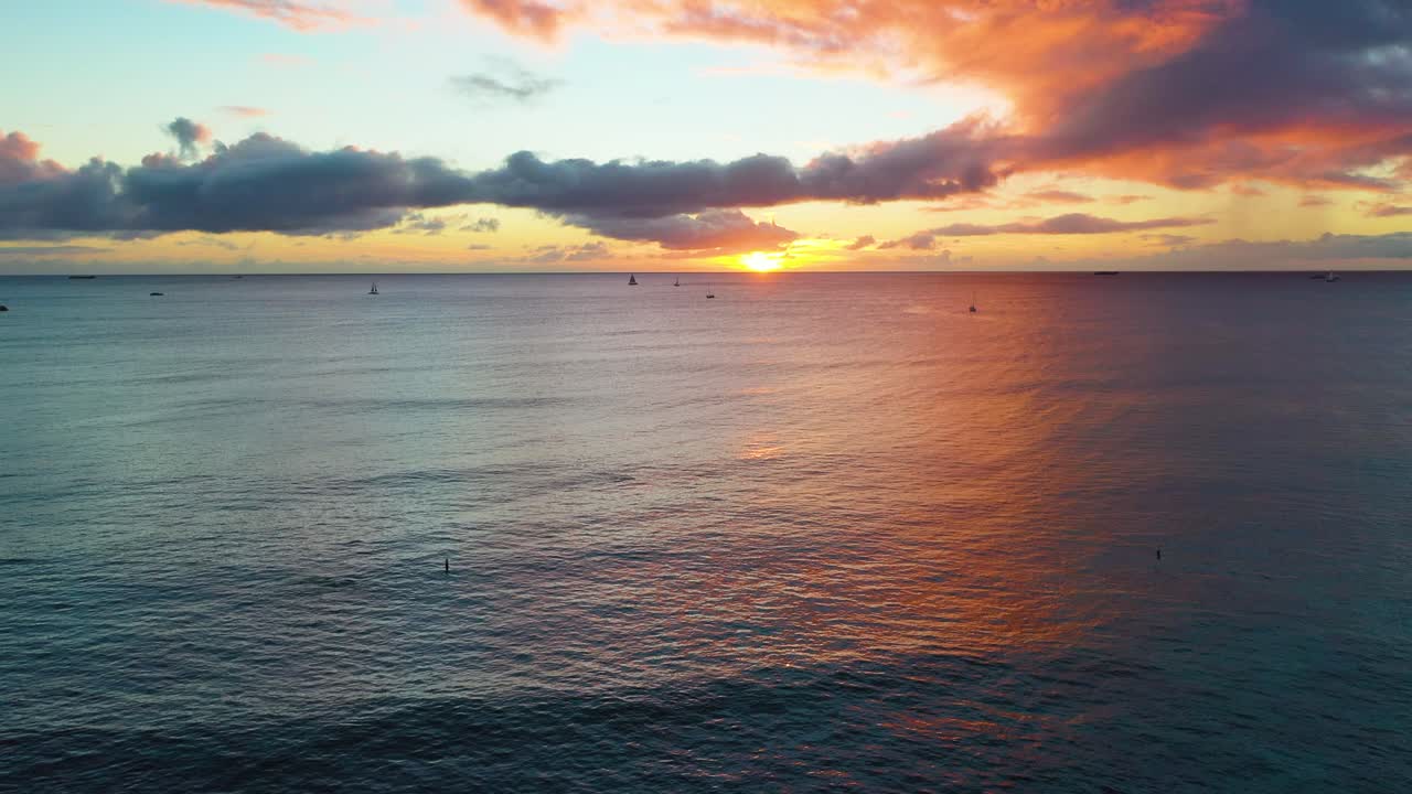 하와이 호놀룰루에 있는 와이키키 해변의 졸졸 흐르는 파도 속에서 범선과 서퍼들 위로 떠오르는 태양