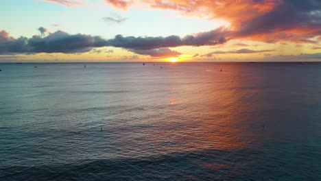 sun rising over fleet of sailboats and surfers in the rippling waves of waikiki beach in honolulu, hawaii