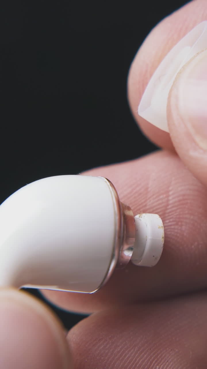 man fingers takes off silicone cup from modern earphone to clean from earwax on black background extreme close view
