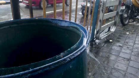 rainwater from the roof falling and splashing at the edge of an empty blue barrel - closeup shot