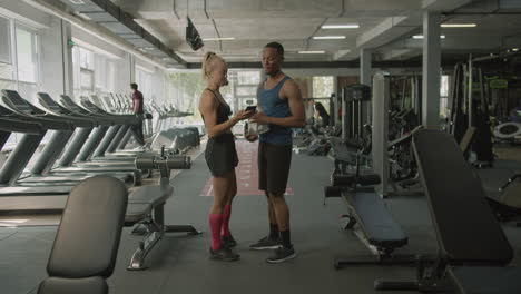 caucasian female monitor and an athletic african american man talking in the gym.