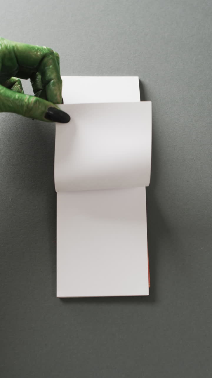 Vertical video of halloween green monster hands and notebook with copy space on grey background