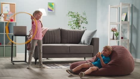 Niños-De-Pelo-Rubio-Relajándose-En-Una-Habitación-Luminosa,-Una-Chica-Sonriente-Está-Girando-Hula-hoop