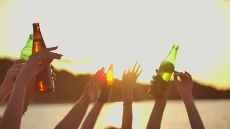 company of young people are dancing with hands up with beer. this is perfect party at sunset on the lake coast.