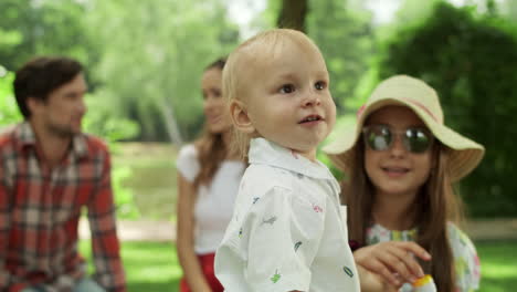 sister and toddler looking at camera outdoors. family relaxing together in park