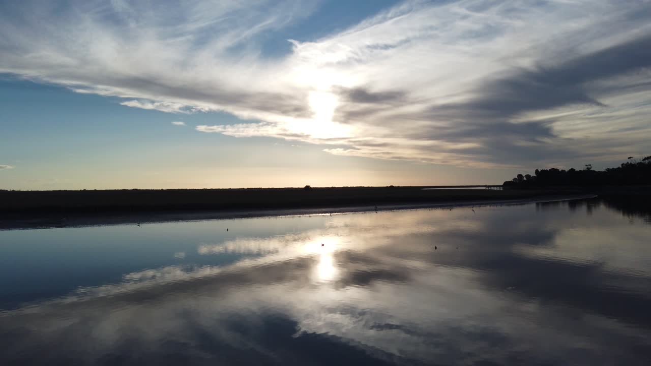 Minimalistický letecký pohled: ústí řeky San Clemente Tuyu, Argentina. Zrcadlová vodní krajina s odrazem slunce.