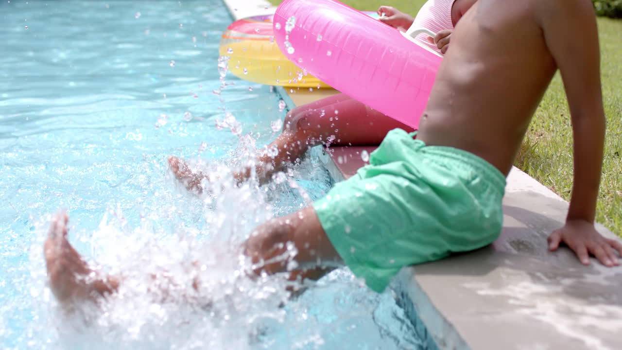 African American siblings splash water by a poolside at home, with a pink float nearby