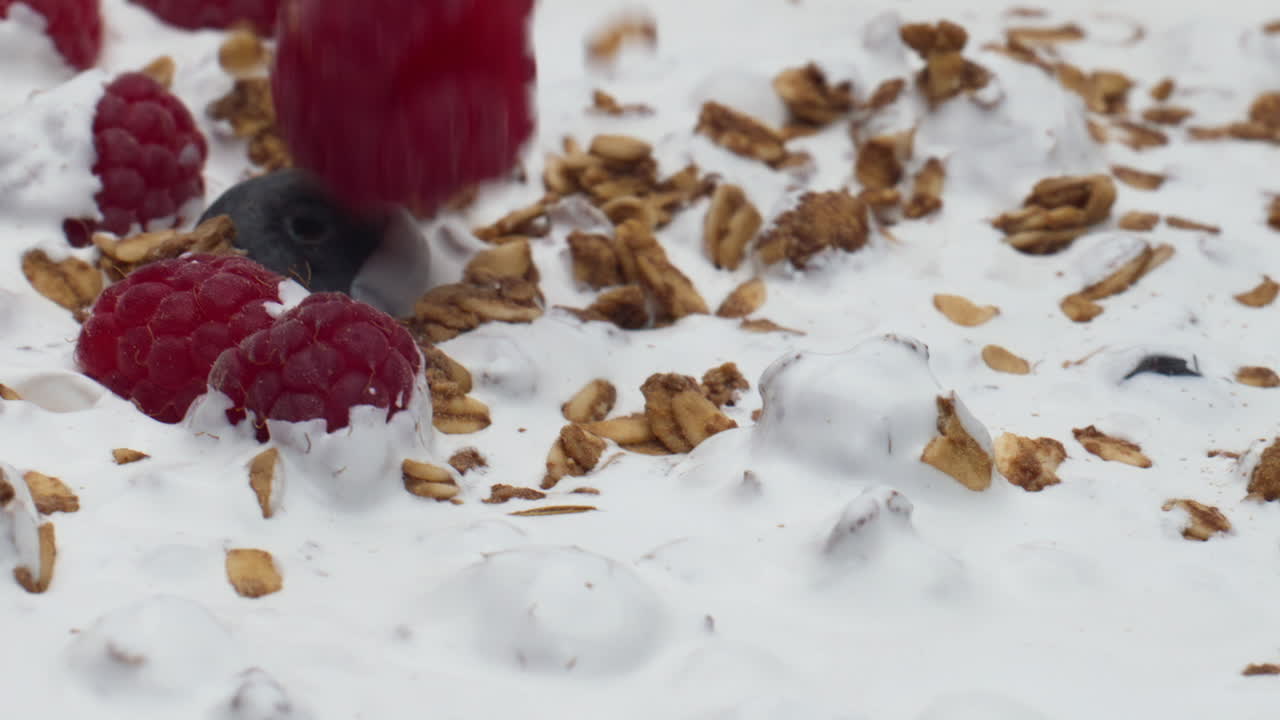Raspberry falling yogurt cereal flakes in super slow motion closeup. Vegan food.