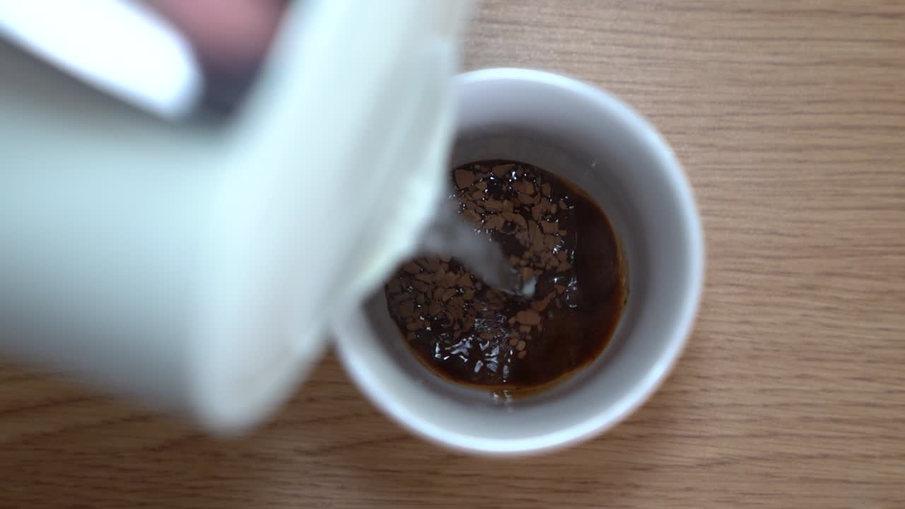 Top-down view of adding hot water to a cup of instant coffee.