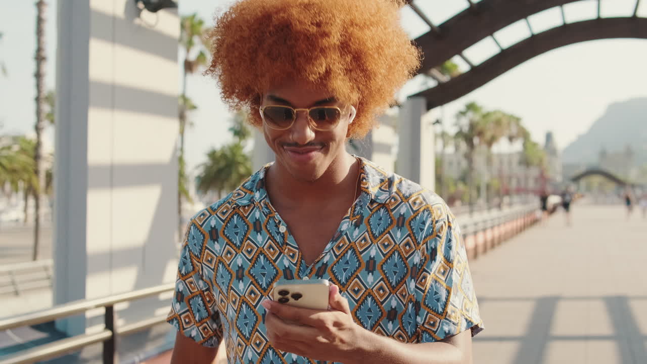 Giovane uomo con capelli ricci che usa lo smartphone e sorride all'aperto