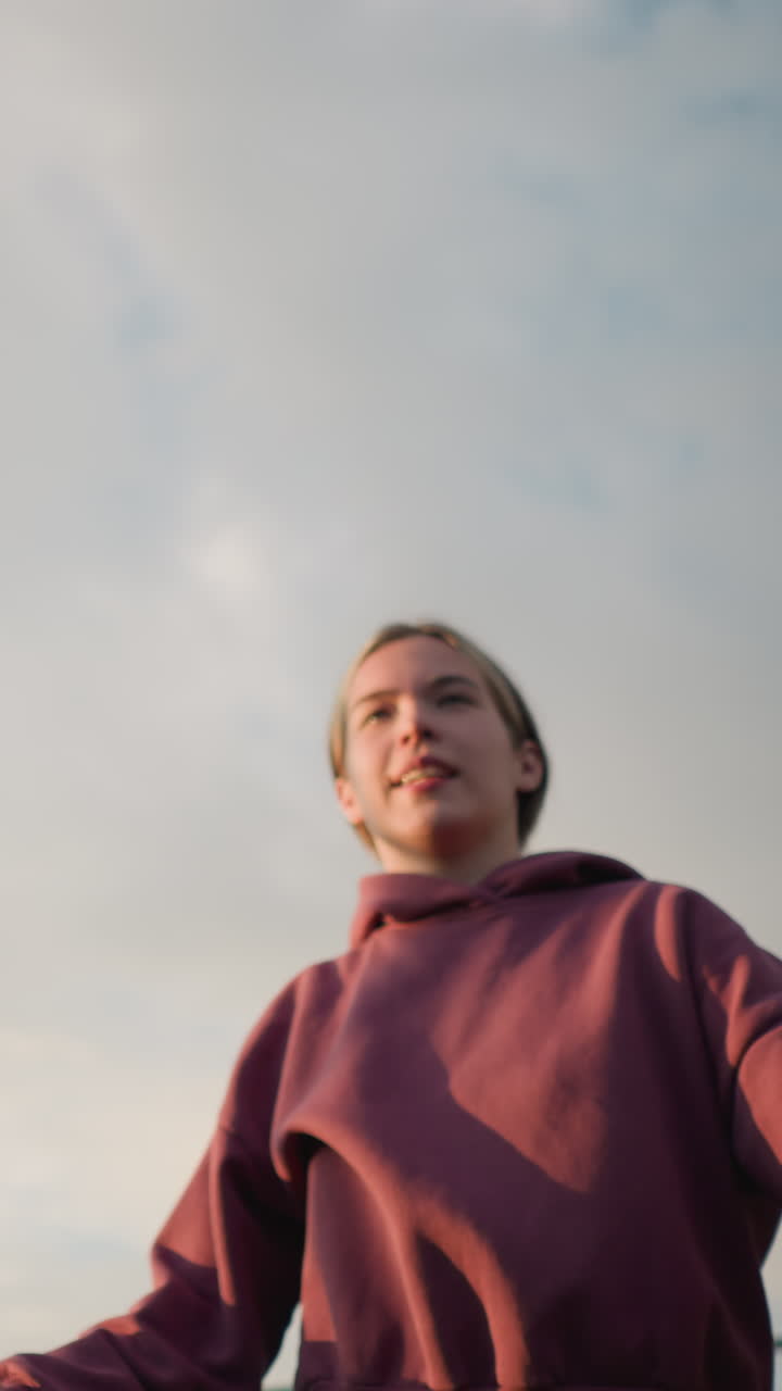 primer plano de una mujer con capucha sirviendo voleibol al aire libre, preparándose para servir con una fuerte acción de brazo en el campo abierto con cielo brillante y vegetación sutil en el fondo