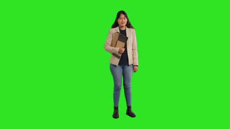 full length studio portrait of female teacher or businesswoman standing against green screen carrying folder